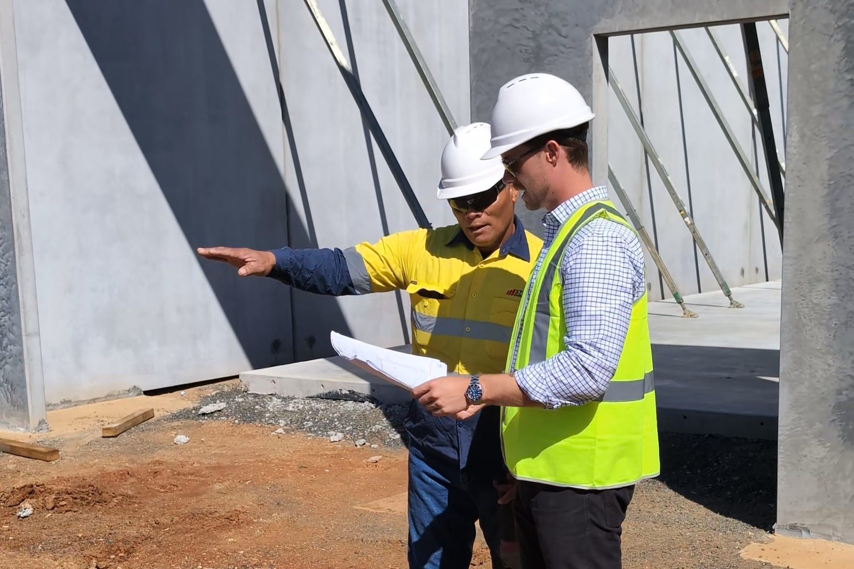 Jack Chaffey on an active commercial development site reviewing plans with a Stripes Group site supervisor in front of tilt-up concrete panels